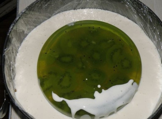 1. Этап. Чизкейк с киви без выпечки: Разводим желатин для киви с готовым желатином со вкусом киви. Оставляем застывать в форме поменьше, добавляем нарезанные фрукты. Молоко смешиваем с желатином и оставляем набухать. Ставим на огонь, ждем, пока желатин растает. После соединяем молоко со сметаной и сахаром. Застывшую киви-массу выкладываем на слой печенья и заливаем остывшей молочно-желатиновой смесью.