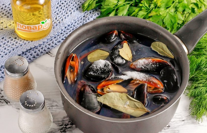 1. Этап. Мидии, запеченные с сыром в духовке: Промойте мидии, выложите их в казан, кастрюлю или ковш с антипригарным дном и залейте кипятком. Добавьте соль и лавровые листья. В кипятке ракушки раскроются, так и должно быть. Отварите их 3-4 минуты с момента закипания жидкости в емкости.