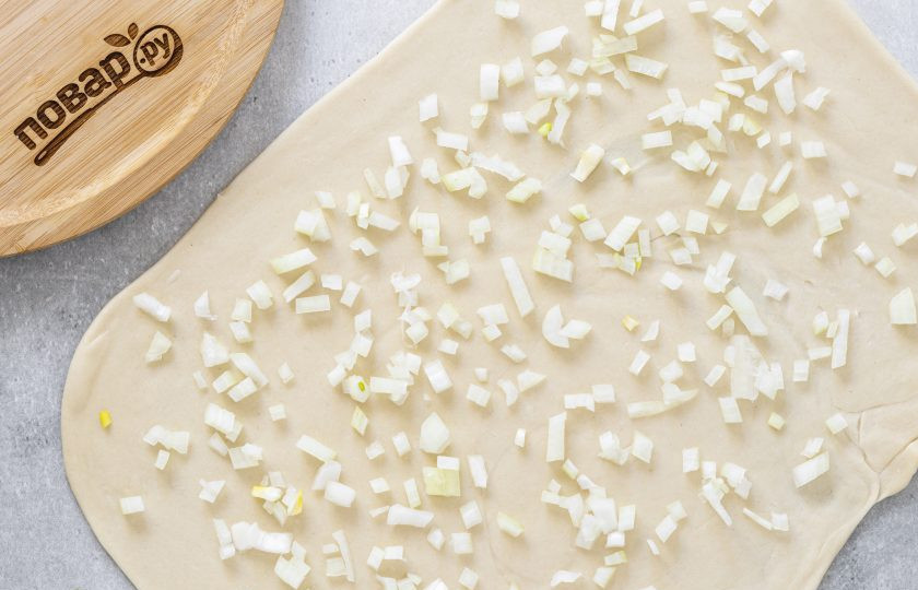 1. Этап. Лепешки на воде с луком: Снова раскатайте тесто в тонкий прямоугольный пласт. Репчатый лук нарежьте на маленькие кубики. Выложите их на тесто и слега вдавите.