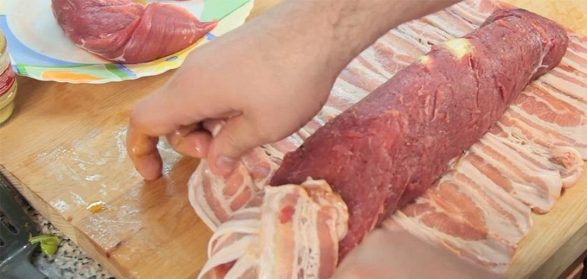 1. Этап. Мясной рулет с морковью: Выложите на мясо плавленый сыр, затем морковь и последним слоем — лук. Аккуратно сверните рулет. Затем укройте рулет беконом, укладывая полоски внахлест. Закрепите зубочистками бекон.