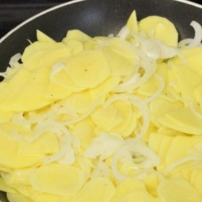 1. Этап. Испанская тортилья: 3. Нагрейте пару ложек оливкового масла в сковороде и выложите картофель с луком. Огонь понизьте до среднего и накройте сковороду крышкой. Жарьте картофель под крышкой, периодически помешивая, в течение 15 минут.