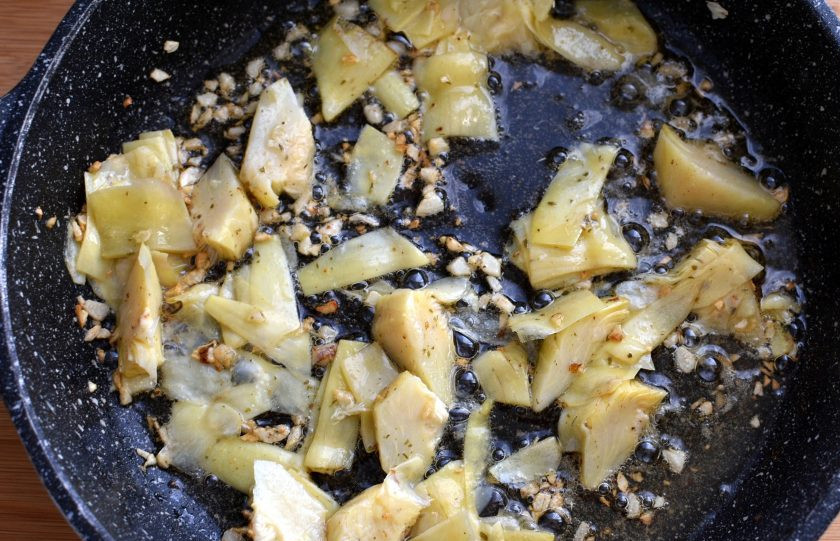 1. Этап. Куриная пикката с артишоком: В сковороду выложите рубленый чеснок и серединки артишока. Быстро обжарьте в течение 1 минуты.