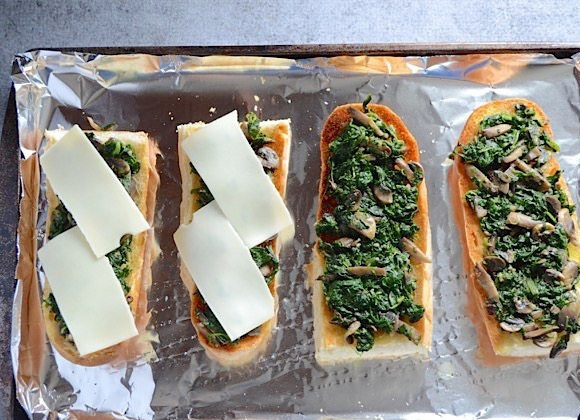 1. Этап. Бутерброды в духовке с грибами и шпинатом: 4. Достаньте хлеб и распределите приготовленную начинку. Уложите поверх начинки сыр.