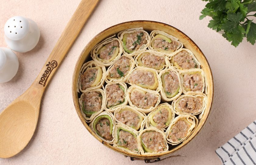 1. Этап. Пирог из лаваша с фаршем и кабачком: Готовый рулет нарежьте на кусочки, шириной около 3-4 см. и выложите их в жаропрочную форму для выпечки, вплотную друг к другу. Дно застелите пергаментом и смажьте маслом.