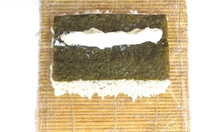 1. Этап. Роллы в духовке: Переверните лист нори рисом вниз и уложите полоску сливочного сыра.