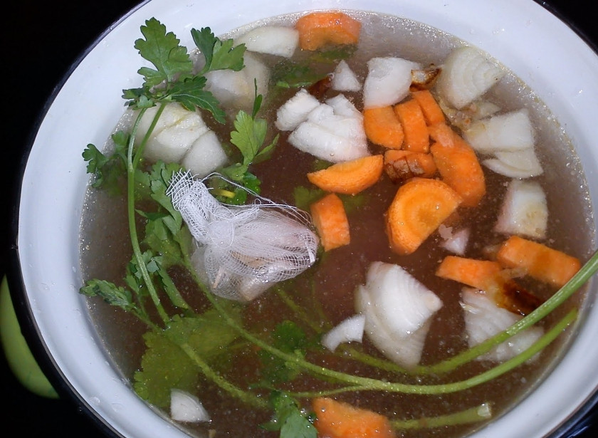 1. Этап. Свиной бульон: 3. На огонь ставим кастрюлю, перекладываем в неё печеные овощи с мясом, добавляем остальные сырые овощи, на противень наливаем теплой воды, размешиваем и переливаем в кастрюлю. Наливаем воду, чтобы она на 3 пальца покрывала кости с овощами, добавляем половину всей петрушки, в марлю заворачиваем гвоздику и перец, и добавляем её в кастрюлю вместе с лавровым листом. Доводим до кипения, после чего варим на минимальном огне 2-3 часа, снимая пену. Бульон готов, солим и подаем его с рубленой зеленью.