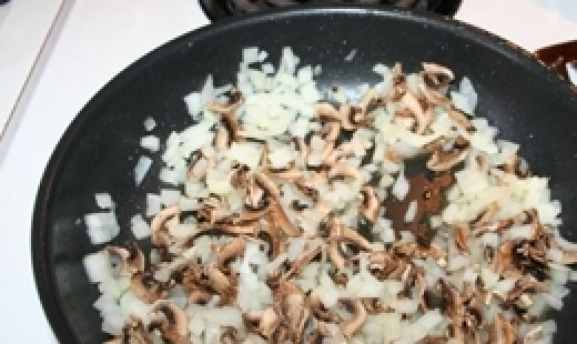 1. Этап. Кролик тушеный в горшочке: Когда жидкость из них полностью выкипит грибы начнут румяниться, добавить нарезанный лук. Обжаривать до золотистого цвета.