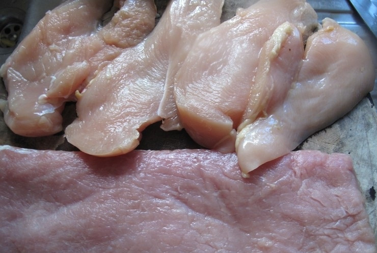 1. Этап. Курица со свининой в духовке: 1. Мясо моем и высушиваем бумажным полотенцем. Нарезаем курицу и свинину тонкими кусочками. Застилаем мясо пищевой пленкой и немного отбиваем, чтобы оно получилось нежным и сочным.