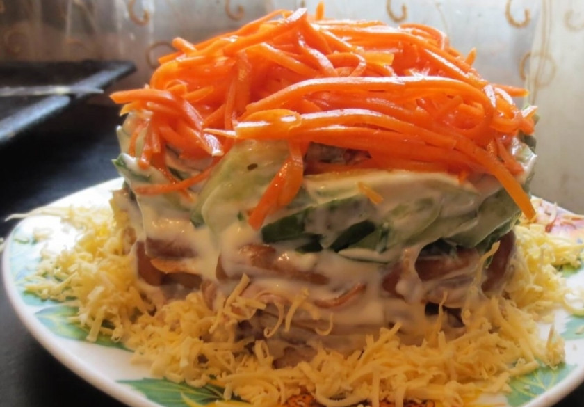 1. Этап. Салат с курицей, и грибами, и огурцами: Верхушку салата украсьте корейской морковью. Сбоку присыпьте тертым сыром. Поместите форму с салатом в холодильник на несколько часов. Затем аккуратно удалите форму и подавайте салат к столу. Приятного аппетита!