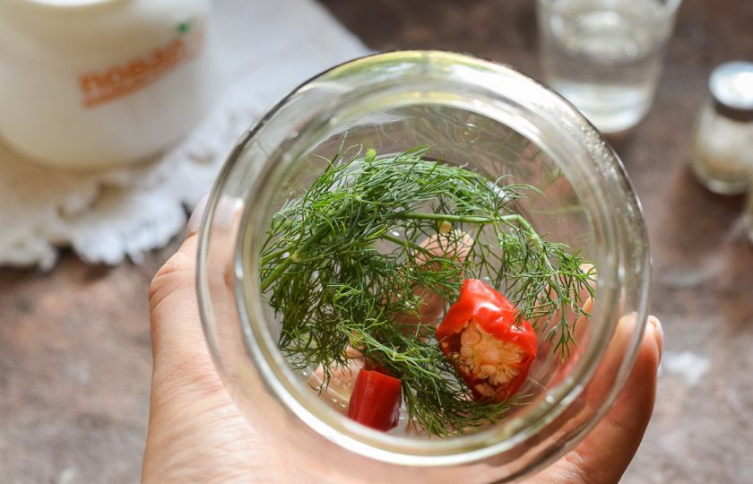 1. Этап. Консервированные помидоры чили на зиму без стерилизации: Банку для заготовки тщательно вымойте с пищевой содой, после ополосните хорошо под теплой проточной водой. Стерилизуйте банку удобным способом – над паром, в духовке или микроволновке. Крышку опустите в воду и проварите 10 минут. Переложите в банку укроп, чеснок и чили.