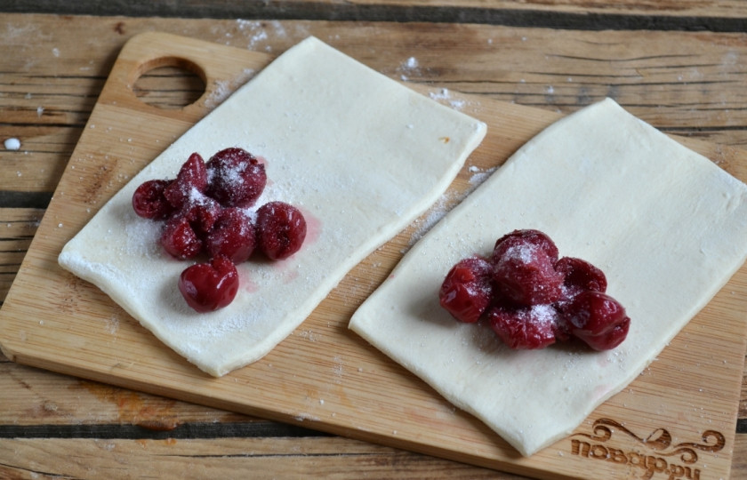 1. Этап. Слойки с вишней из слоеного теста: Положите внесколько ягод вишни и присыпьте сахаром.