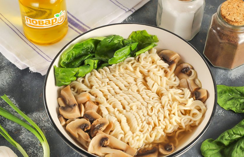 1. Этап. Рамен с сыром: Промойте листья шпината и срежьте стебли. Выложите их в емкость с лапшой. По желанию шпинат можно заменить пекинской капустой. Влейте в бульон соевый соус.