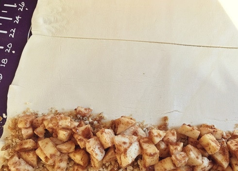 1. Этап. Штрудель яблочный из готового слоеного теста: Высыпаем на один пласт теста, отступив от края примерно 4 см, половину смеси орехов и сухарей, а поверх выкладываем половину яблок. Второй штрудель делаем точно так же.