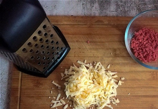 1. Этап. Слойки с колбасками и сыром: Натираем сыр на тёрке средней величины. Отправляем к колбаскам.