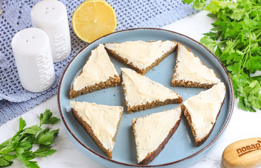 1. Этап. Канапе с селедкой и лимоном: Предпочтительнее приобретать квадратный тостовый хлеб или хлеб-кирпичик. Разрежьте его по диагонали и еще раз по диагонали, получая небольшие треугольники. Обмажьте их сливочным сыром и выложите на тарелку. Можно заменить сливочный сыр плавленым.