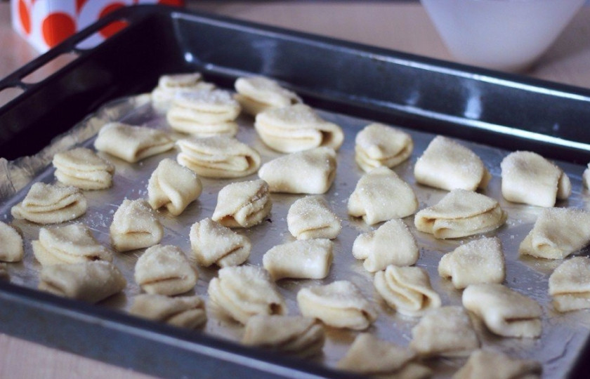 1. Этап. Творожное печенье к чаю: В миску или блюдце высыпаем сахар. Обмакиваем кружочек с одной стороны. Сворачиваем пополам (сахаром внутрь) и снова обмакиваем в сахар одной стороной. Этой же стороной внутрь складываем кружок еще раз — и опять окунаем в сахар одной стороной. Повторяем действия со всеми кружками. Противень застилаем бумагой для выпечки или фольгой (можно немножко смазать маслом). Выкладываем наши будущие печеньки сахарной стороной вверх.