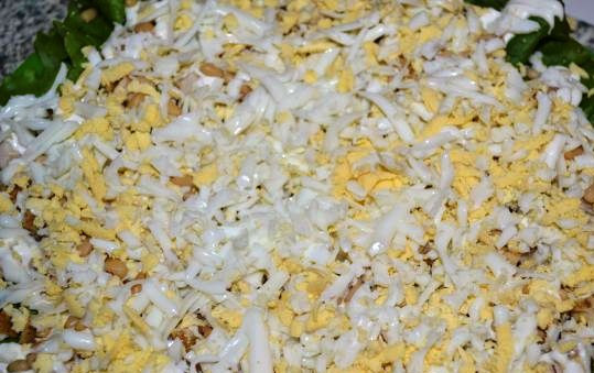 1. Этап. Салат Тиффани: Яйца отварите и потрите на крупной терке. Посыпьте мясо кедровыми орешками, выложите яйца.