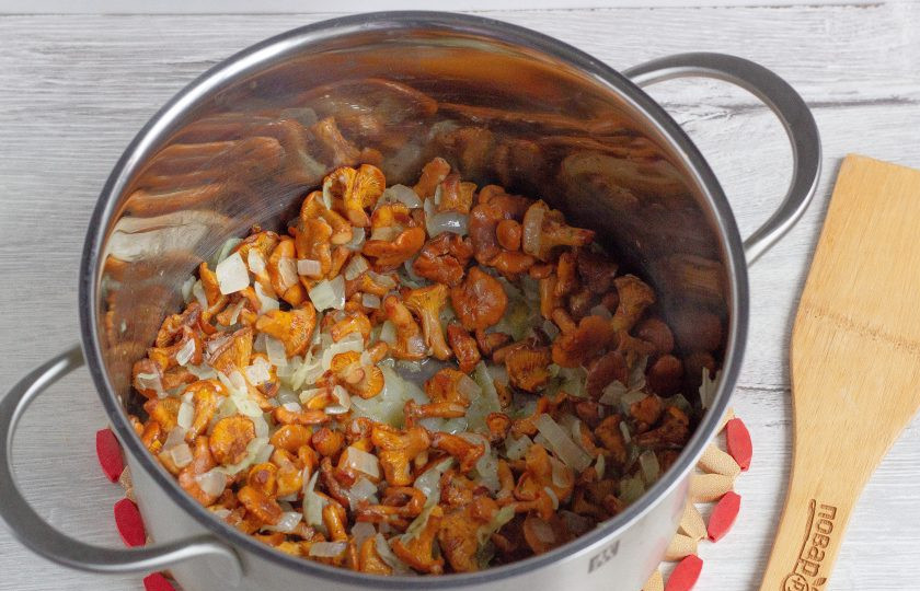 1. Этап. Деревенский суп с лисичками: Поставьте на плиту кастрюлю с толстым дном, добавьте туда 2 вида масла и обжарьте в нем нарезанный лук до прозрачности (1,5 головки, половинку лука отложите). Затем добавьте грибы. Посолите по вкусу, добавьте орегано и тушите около 5 минут на среднем огне.