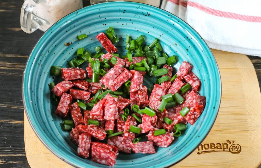 1. Этап. Салат с яичными блинчиками и луком: Копченую колбасу, ветчину или отварное мясо нарежьте брусочками. Промойте перья зеленого лука, измельчите и высыпьте в глубокую емкость вместе с колбасной нарезкой.