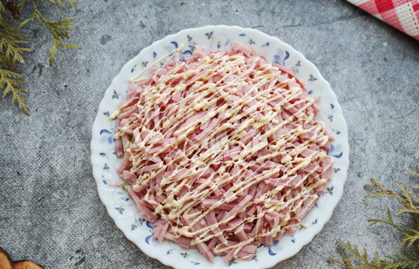 1. Этап. Салат Орхидея с чипсами и ветчиной: Ветчину порежьте тонкой, не длинной соломкой и выложите поверх чипсов. Сделайте сеточку из майонеза.