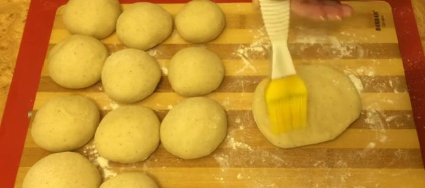 1. Этап. Сдобные рогалики с кунжутом: 4. Разделите тесто на 12 частей и присыпьте их мукой. Каждой части придайте форму колобка и разомните в лепешку. Смажьте лепешку растительным маслом, посыпьте белым и черным кунжутом.