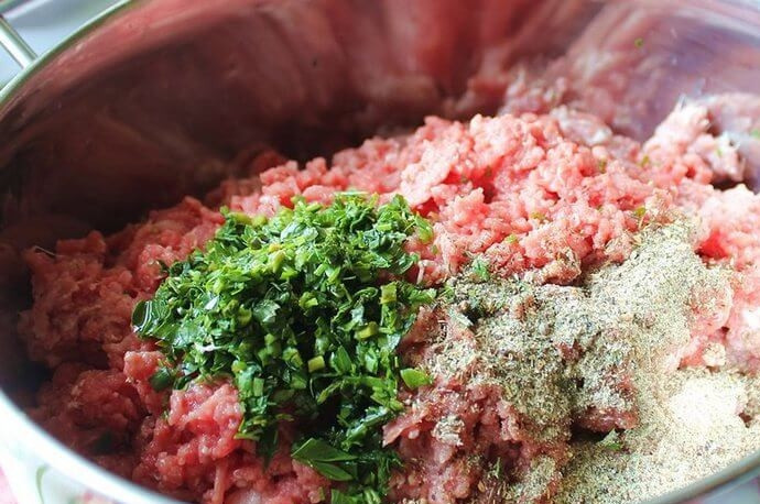 1. Этап. Колбаски из свинины: Очистите и нарежьте лук. Измельчите мясо в мясорубке вместе с луком. В зависимости от желаемой консистенции и плотности колбасок можете перемолоть его два раза. Добавьте мелко нарубленную зелень, приправы и специи.