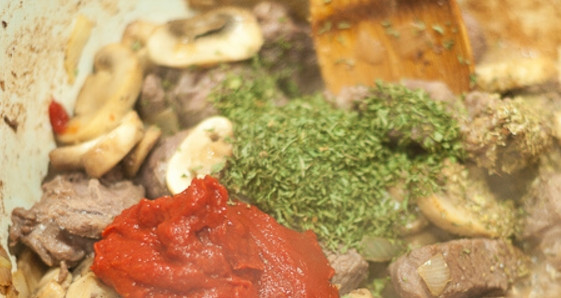 1. Этап. Мясо, тушенное с грибами: 6. Влейте говяжий бульон (или воду), добавьте томатную пасту, петрушку и орегано, доведите содержимое до кипения, затем тушите на слабом огне около 1 часа.