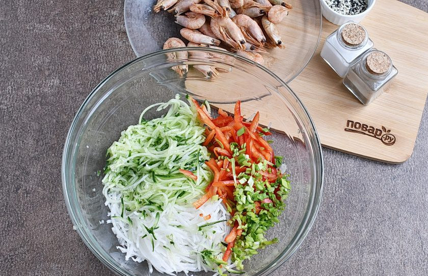 1. Этап. Китайский салат с креветками: Овощи вымойте и обсушите. Дайкон очистите и натрите на терке для корейских салатов. Выложите в просторную миску. Туда же натрите огурец (или нарежьте тонкой соломкой), добавьте сладкий перец соломкой и шинкованный зеленый лук, оставив немного для украшения.