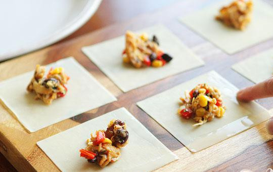 1. Этап. Конвертики с овощной начинкой: 5. Смочить два края каждого квадрата водой и запечатать, чтобы получился треугольник. Осторожно прижать конвертики пальцами, чтобы вышел лишний воздух.