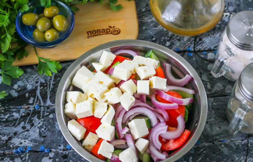1. Этап. Салат с сыром Сиртаки: Очистите от шелухи красную луковицу, промойте в воде и разрежьте пополам. Половину нарежьте полукольцами и высыпьте в емкость. Сыр 