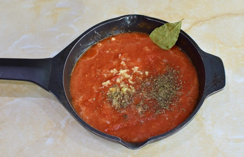1. Этап. Классический соус Маринара: Сразу в сковороду пропустите через пресс пару зубчиков чеснока. Добавьте соль, специи и сушеный базилик. Добавьте лавровый лист.