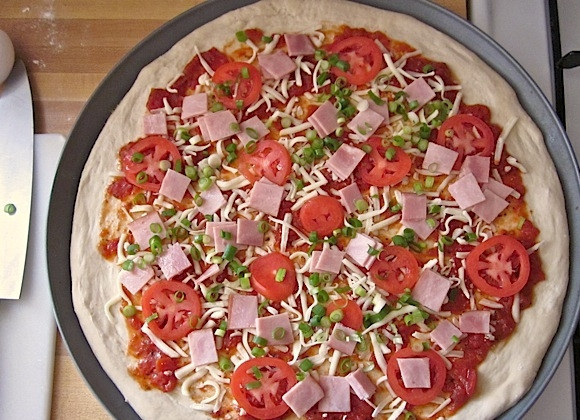 1. Этап. Пицца к завтраку: 5. Посыпьте тесто половиной тертого сыра, положите сверху помидоры, ветчину и зеленый лук.
