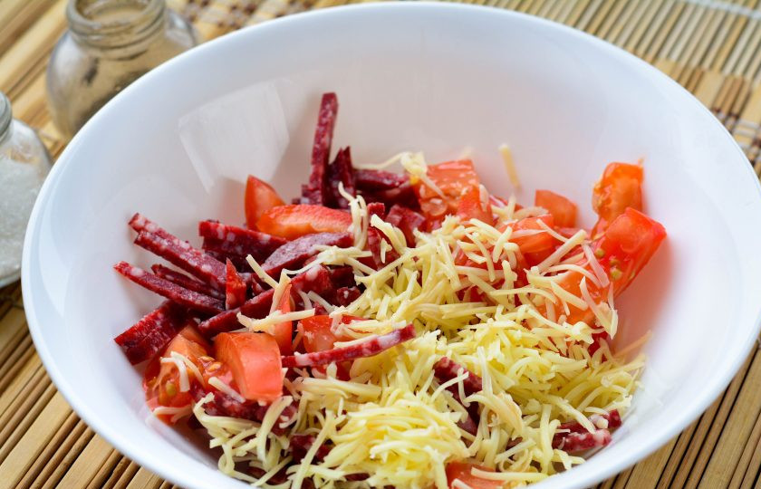 1. Этап. Грузинский салат с колбасой и помидорами: Смешайте в миске все нарезанные компоненты салата - сыр, колбасу и помидоры.