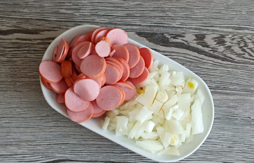 1. Этап. Солянка на говяжьем бульоне: Нарежьте лук мелким кубиком. Сосиски — кружками.