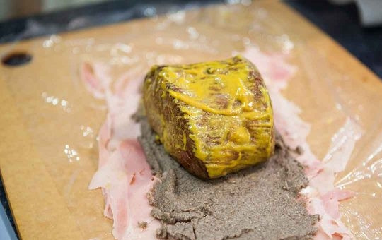 1. Этап. Говядина в горчице и слоеном тесте: 3. Возьмите пищевую пленку, выложите на нее тонко нарезанные ломтики ветчины, затем выложите слой из грибного паштета, а уже сверху выложите мясо.