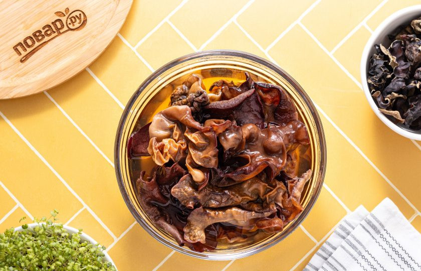 1. Этап. Салат из фунчозы и китайских древесных грибов: Древесные грибы заранее замочите в горячей воде на 1 час или больше. После слейте воду, а грибы тщательно промойте в чистой воде несколько раз — на них может быть земля и мусор. Отрежьте плодоножки со всех грибов. Нарежьте грибы соломкой.