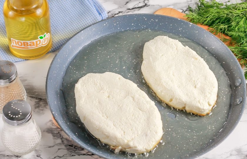 1. Этап. Ленивый творожный хачапури по-аджарски на сковороде: Разделите творожную массу на две равные части и вылепите из них заготовки в виде лодочек. Прогрейте в сковороде растительное масло и выложите в него заготовки. Нагрев убавьте до умеренного и обжарьте с одной стороны примерно 2-3 минуты.