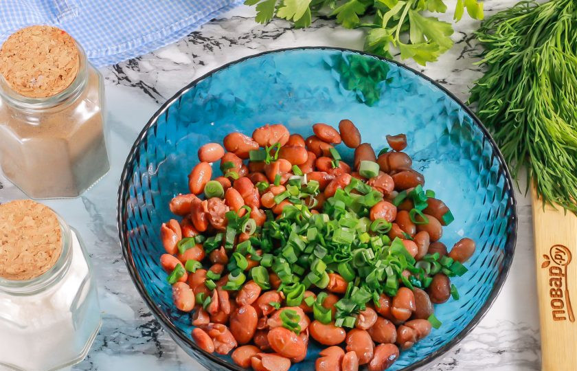 1. Этап. Салат с фасолью, сосисками, сыром и сухариками: Отварную или консервированную фасоль выложите в глубокую емкость. Промойте стебли зеленого лука и измельчите. Добавьте к фасоли.