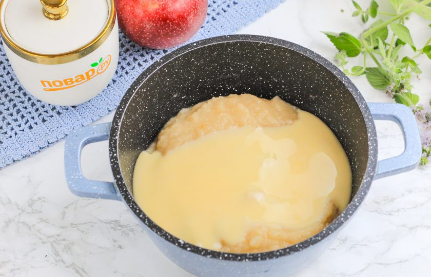 1. Этап. Пюре Лакомка: Выложите яблочное пюре в казан или ковш с антипригарным дном, долейте сгущенное молоко. По желанию можно добавить ванильный сахар или молотую корицу. Перемешайте и поместите емкость на плиту, включая умеренный нагрев.