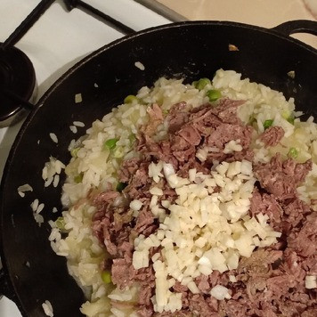 1. Этап. Кабачки, фаршированные рисом и тушенкой: Выложить мясо в сковороду к рису и посыпать рубленым чесноком.