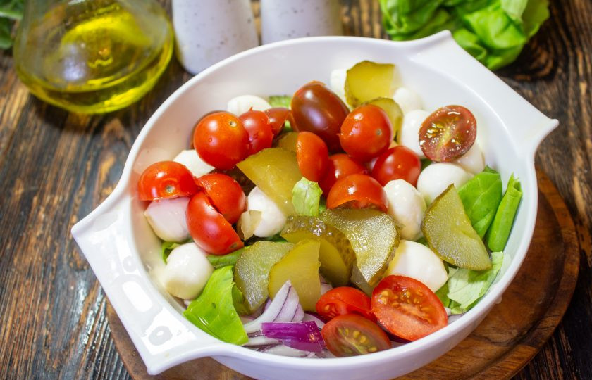 1. Этап. Салат с маринованными огурцами, помидорами и сыром: Помидоры черри нарежьте пополам, а огурцы на кусочки. Добавьте овощи в салатник.