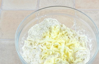 1. Этап. Пирог из песочного теста с замороженными ягодами: Вначале сделайте тесто. Муку смешайте с сахаром. К ним натрите подмороженное масло на крупной тёрке.