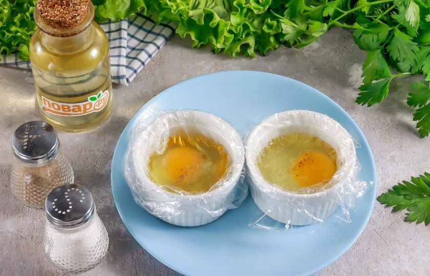1. Этап. Тост с авокадо, соленой семгой и яйцом пашот: В пиалы или чашки выложите пищевую пленку, заходя за их края. Обязательно смажьте пленку внутри растительным маслом. Вбейте туда по одному куриному яйцу, посолите и поперчите.