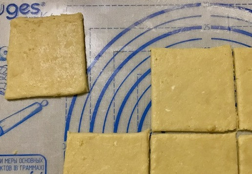 1. Этап. Печенье Вертушки: Разогрейте духовку до 200 С. Застелите противень пергаментной бумагой или силиконовым ковриком для выпечки. Яичный белок взбейте вилкой. Достаньте из холодильника одну порцию теста и на посыпанной мукой рабочей поверхности раскатайте тесто в прямоугольный пласт толщиной примерно 0,4-0,5 мм. Если в процессе раскатки тесто становится слишком мягким, охладите его в холодильнике, затем продолжайте раскатывать. Разрежьте тесто на равные квадраты размером 7-7,5 см (при желании используйте линейку). Работайте очень быстро, так как тесто быстро размягчается.