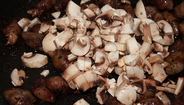 1. Этап. Куриные сердечки в сливках: Когда время будет подходить к концу, нарезаем шампиньоны на небольшие кусочки и выкладываем их на сковороду, жарим все вместе еще минут 5.