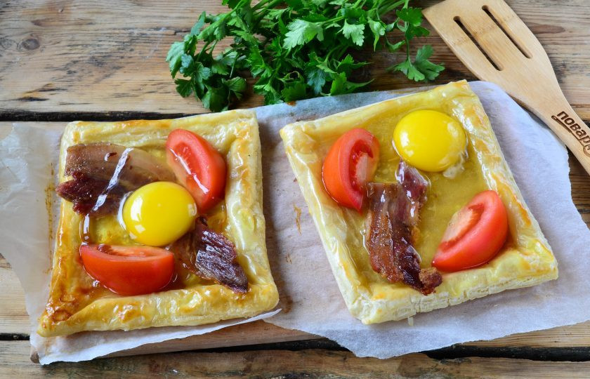 1. Этап. Пикантный слоеный пирог с беконом и глазуньей: Слоеное тесто тем временем почти готово. В середине слегка примните его ложкой, чтобы было удобно выкладывать начинку. Сначала положите горсточку натертого на мелкой терке сыра, затем положите несколько ломтиков и пару полосочек бекона. Разбейте по 1 яйцу и отправьте в духовку, пока яйцо не схватится (еще минут 10-15).