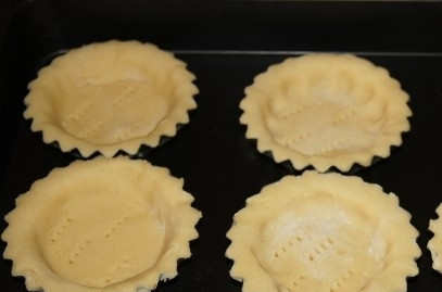 1. Этап. Песочные корзиночки с белковым кремом: Разогрейте духовку до 200 градусов. Достаньте тесто и раскатайте его, отрезая от него по 80г и укладывая кусочки в формочки для выпечки. Серединку проткните вилкой, поставьте корзиночки запекаться на 8 минут в духовку. Потом дайте коржам полностью остыть.