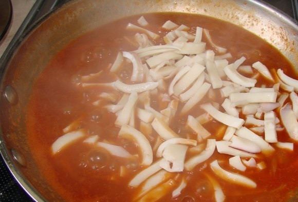 1. Этап. Солянка из морской капусты: Ставим на огонь вок или глубокую сковороду. Наливаем в нее масло, добавляем томатную пасту, обваливаем в муке лук и морковь — и тоже отправляем на сковороду. Сразу же сверху добавляем кальмары, тщательно перемешиваем и выключаем огонь.