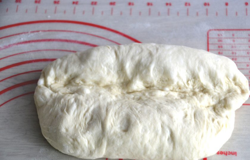 1. Этап. Батон на закваске: Слегка присыпьте рабочую поверхность стола мукой, руками растяните тесто, подверните край теста на 1/3, прищипните.