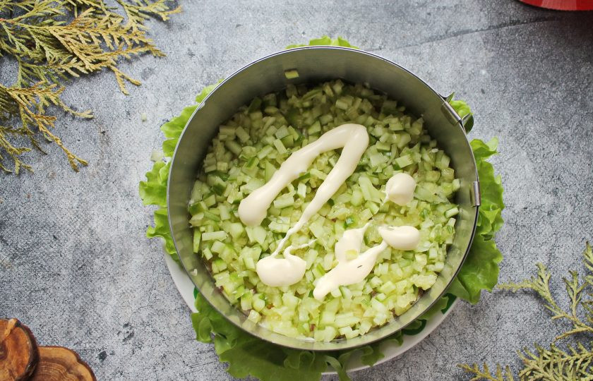 1. Этап. Салат с красной рыбой и креветками слоями: У свежего огурца отрежьте кончики и порежьте мелким кубиком. Если огурец очень сочный, откиньте его на сито и дайте соку стечь. Распределите огурец поверх рыбы, смажьте майонезом.